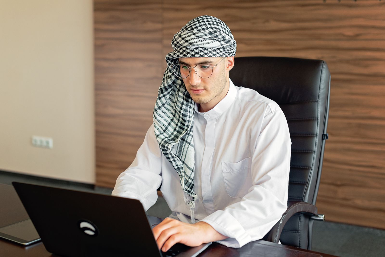 An Arab professional in a white thobe reviewing information on a laptop